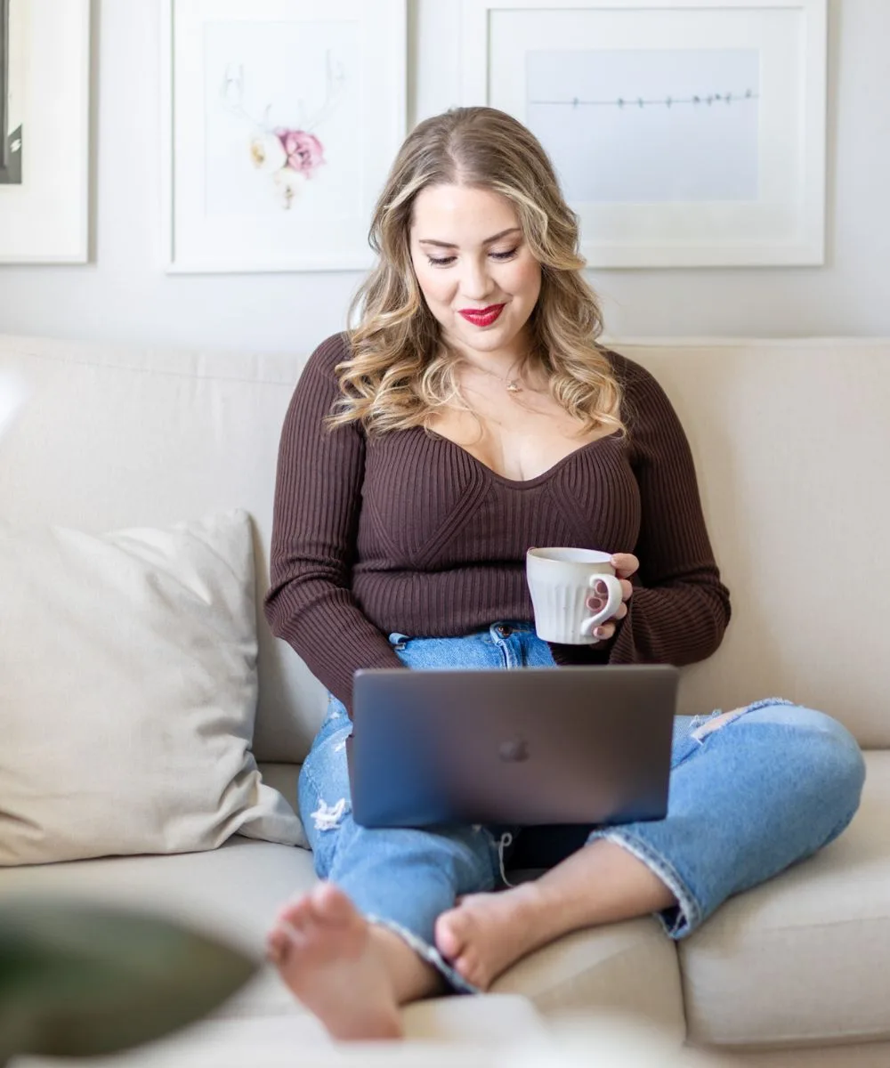 Megan Elliott, founder of The Copy Template Shop, smiling while using her laptop and holding a coffee mug