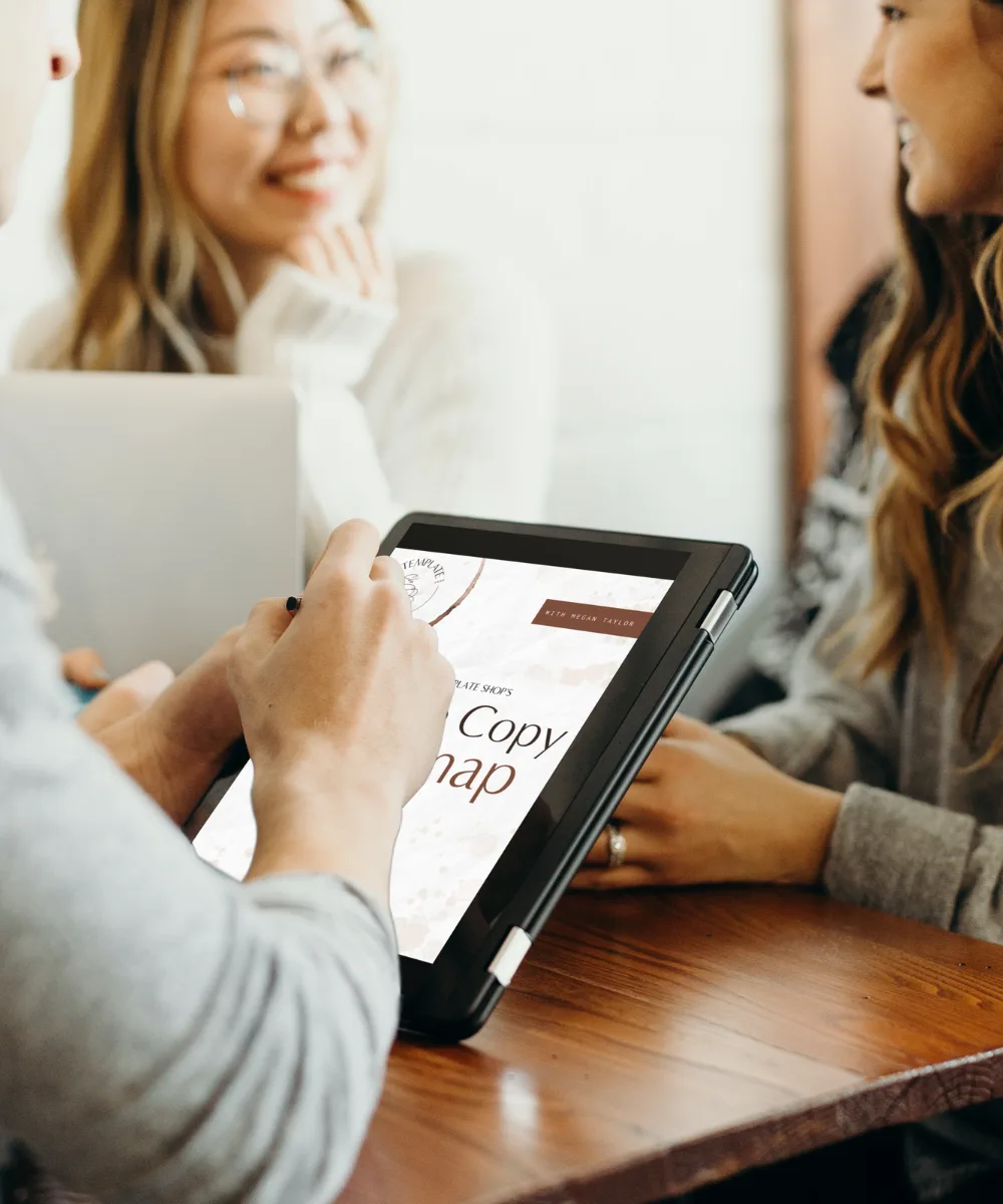women seated around a desk with Free Website Copy Roadmap PDF guide displayed on a tablet
