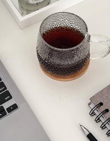 Laptop, glass mug of tea, and spiral notebook on a white desk — a cozy workspace setup for homepage copywriting