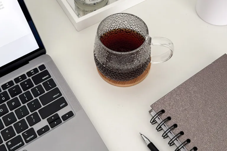 Laptop, glass mug of tea, and spiral notebook on a white desk — a cozy workspace setup for homepage copywriting