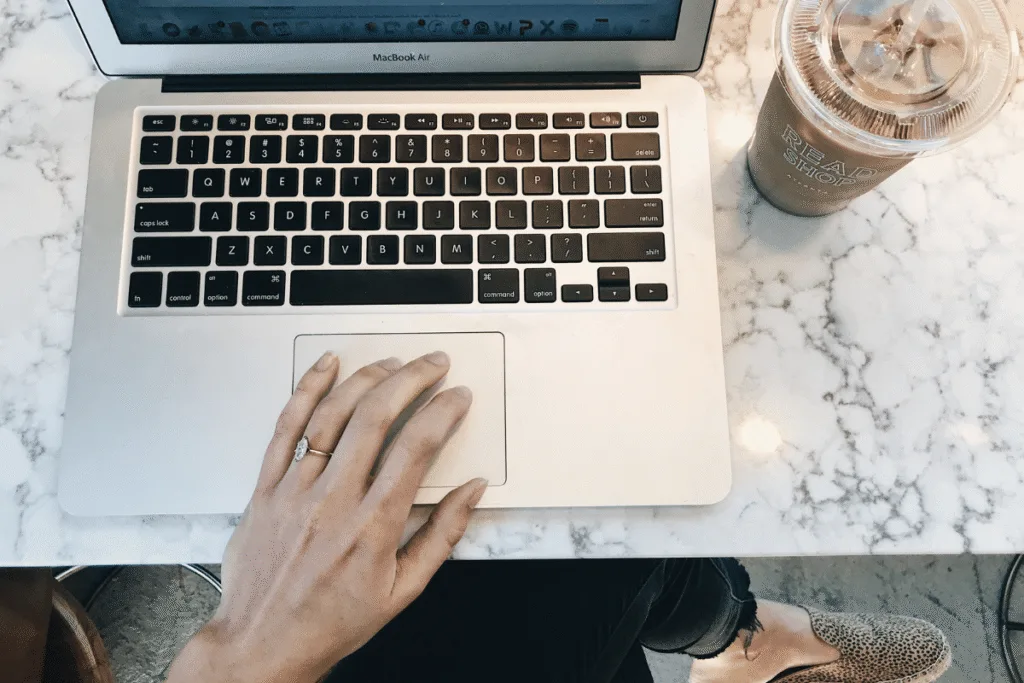 MacBook laptop on a marble table with an iced coffee — working on website copy and SEO strategy for an online service business