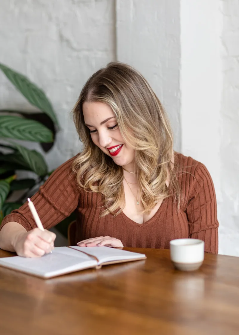 Megan Elliott writing in a journal at a wooden desk with coffee
