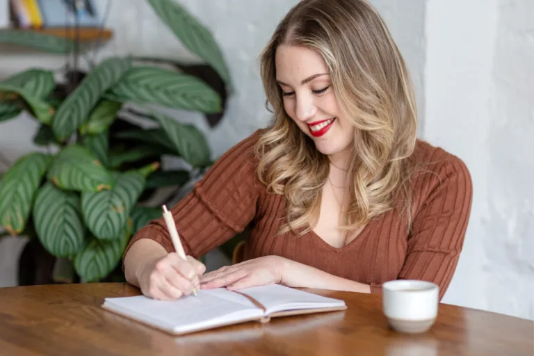 Woman smiling while writing in a notebook at a desk — how to write an about page that connects with clients