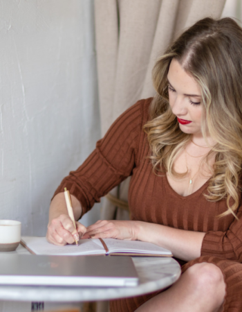 Woman writing in a notebook at a café table — should I write my own website copy or hire a copywriter