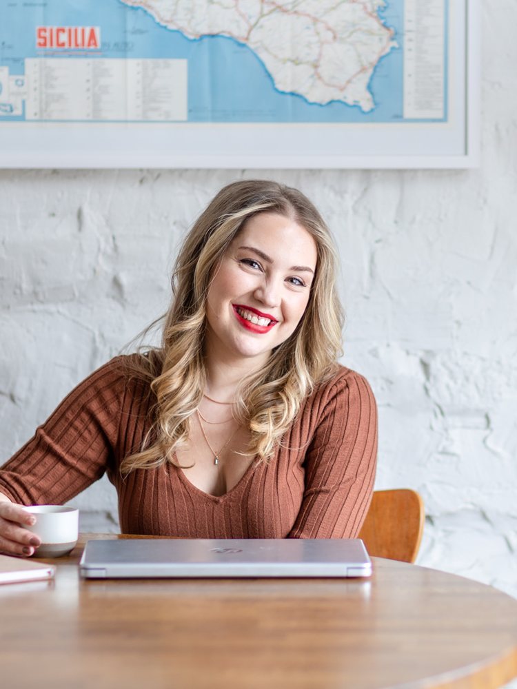Megan smiling at a café table with a cup of coffee and her laptop